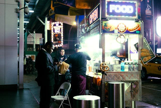 foto de un puesto callejero de comida rápida de noche con clientes consumiendo y hablando